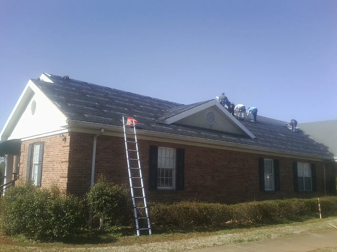 Crew tearing shingles off a brick ranch roof with a ladder set — Emergency Roof Repair work by our crew in Alden