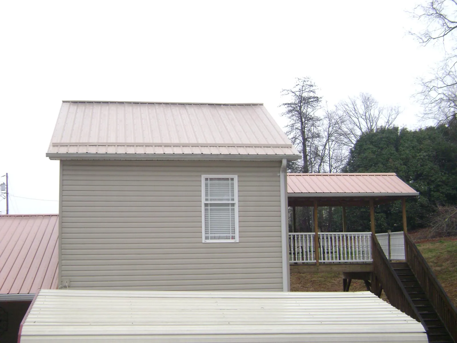 Tan metal roofs on a two story addition and attached porch, from a Roof Replacement job in Alden